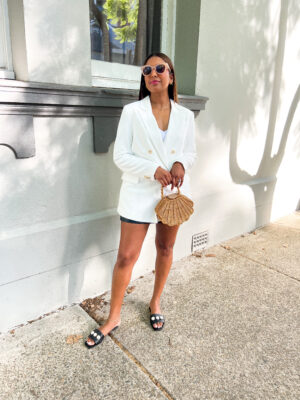 Tina posing with a wicker shell bag. She is wearing a white blazer, and pearl trim slides