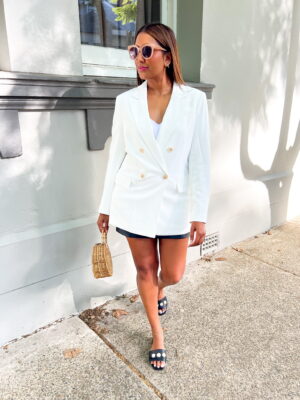 Tina pictured walking towards camera, styled in a white blazer, black skirt and pearl trim slides.